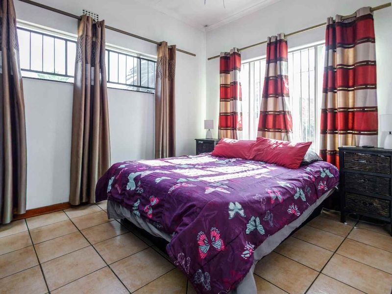 A bedroom featuring tiled flooring and windows fitted with security bars, providing natural light and ventilation.