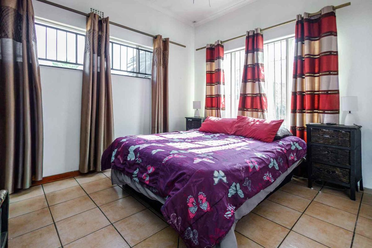 A bedroom featuring tiled flooring and windows fitted with security bars, providing natural light and ventilation.