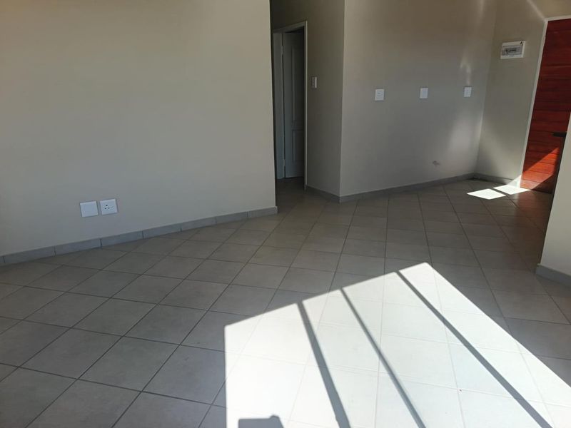 A bright, empty living area featuring neutral tiled flooring and clean wall finishes, providing a versatile blank canvas for interior design.