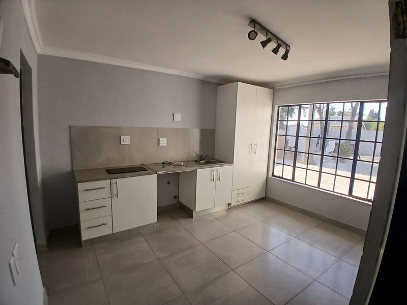 A clean, modern kitchen featuring white cabinetry, tiled flooring, a built-in hob, and a large window providing ample natural light.