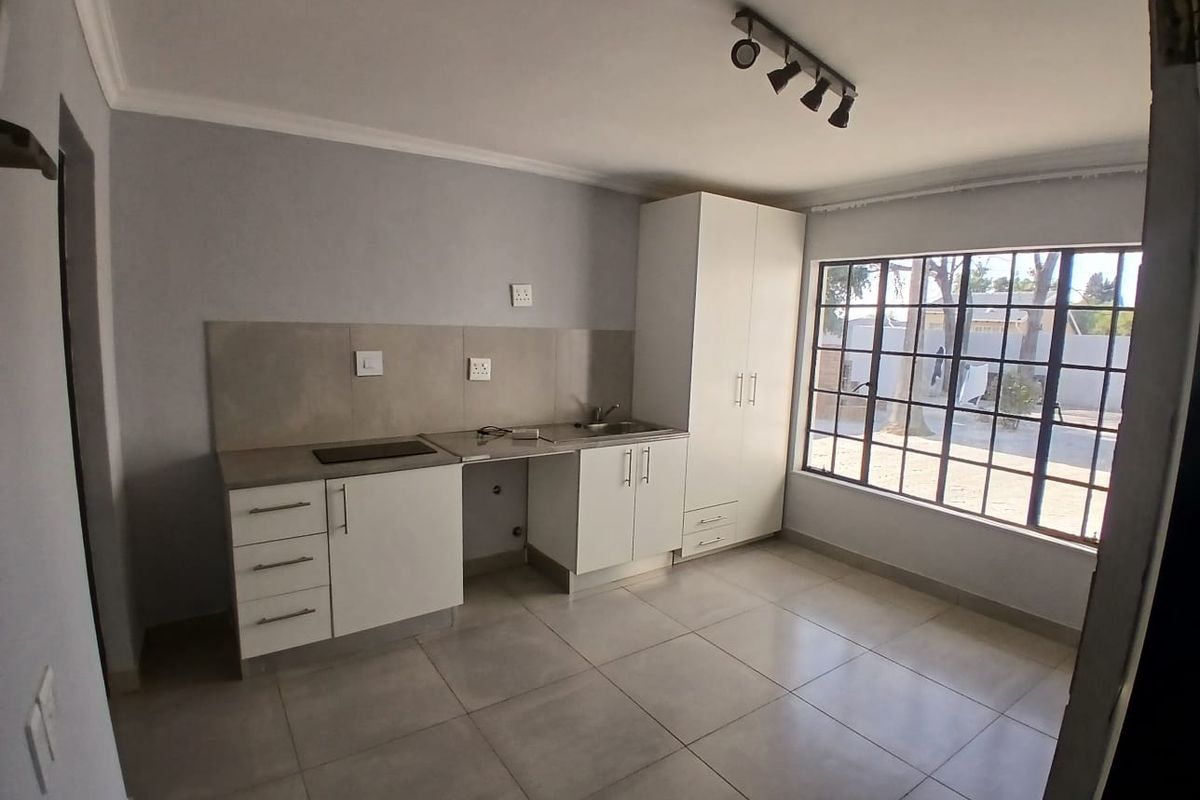 A clean, modern kitchen featuring white cabinetry, tiled flooring, a built-in hob, and a large window providing ample natural light.