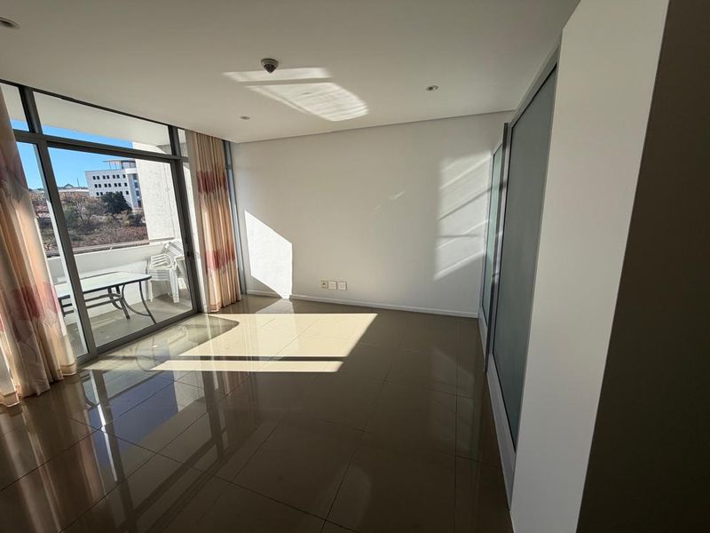 A bright, empty living area featuring polished tile flooring, built-in storage, and large sliding glass doors leading to an outdoor balcony.