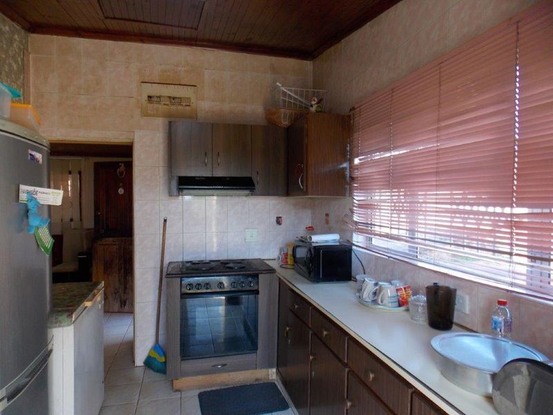 A functional kitchen featuring built-in cabinetry, an electric stove with extractor fan, and tiled splashbacks, requiring cosmetic updates to modernize the space.
