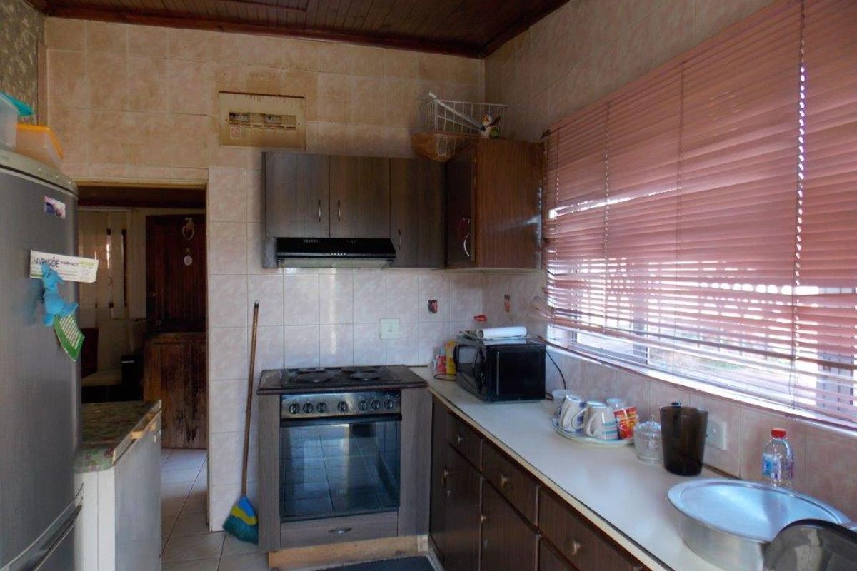 A functional kitchen featuring built-in cabinetry, an electric stove with extractor fan, and tiled splashbacks, requiring cosmetic updates to modernize the space.