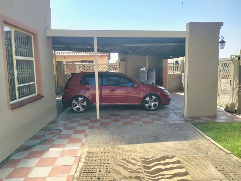 A covered carport area featuring tiled flooring and security features, providing sheltered parking space adjacent to the main house structure.