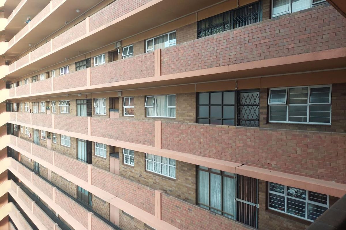 Exterior view of a multi-story apartment building featuring a brick facade with multiple balconies and security-fitted windows.