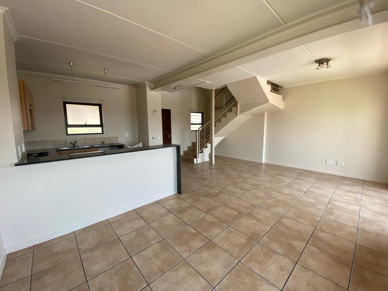 Spacious open-plan living area featuring tiled floors, a functional kitchen with granite countertops, and an internal staircase leading to the upper level.