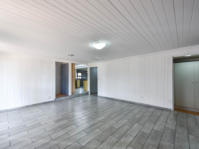 A spacious, empty living area featuring white vertical wall paneling, a matching tongue and groove ceiling, and modern grey ceramic tile flooring.
