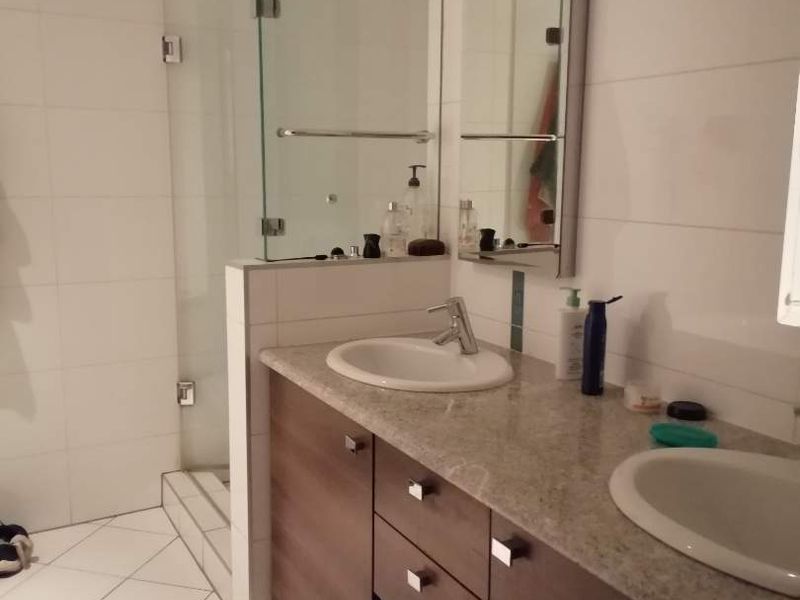 Modern bathroom featuring a double vanity with stone countertop, undermount sinks, and a glass-enclosed shower with tiled finishes.