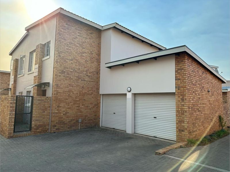 Front view of a modern townhouse featuring a double garage with roller shutter doors, brick and plaster facade, and a paved driveway.