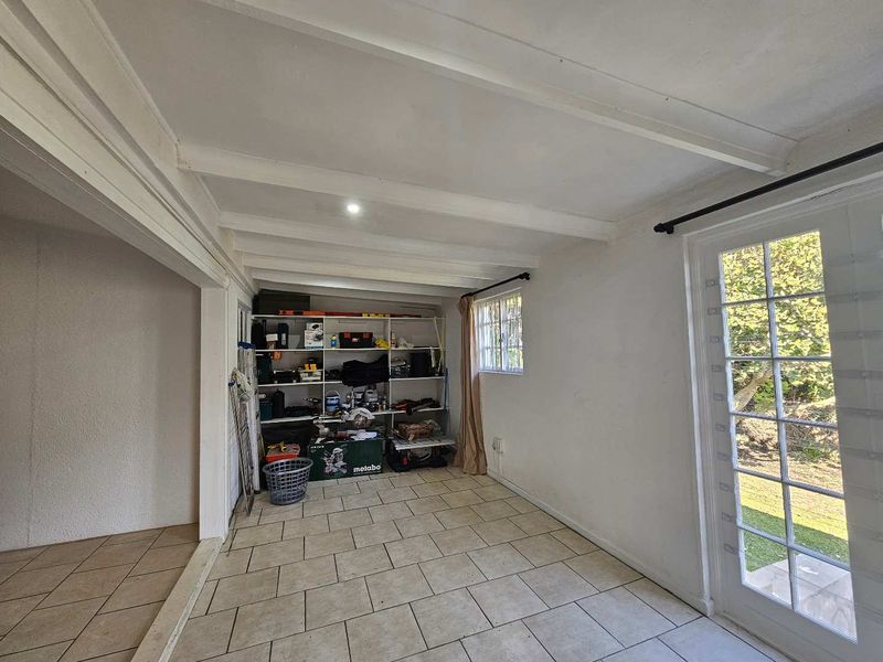 A functional utility space featuring tiled flooring, exposed beam ceilings, built-in storage shelving, and direct access to the garden through french doors.