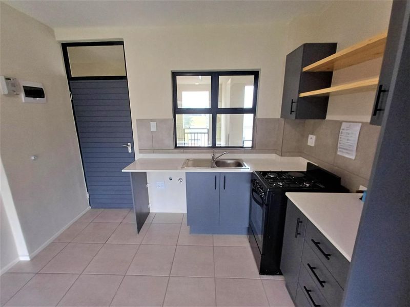 Modern kitchen featuring dark grey cabinetry, open shelving, a gas stove, double bowl sink, and neutral tiled flooring.