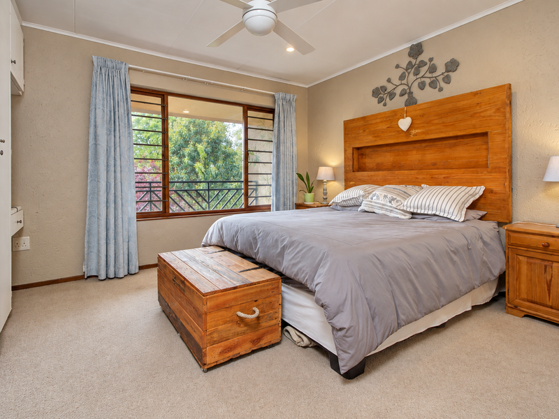A well-maintained bedroom featuring neutral walls, carpeted flooring, a ceiling fan, and a built-in wardrobe with access to a balcony view.