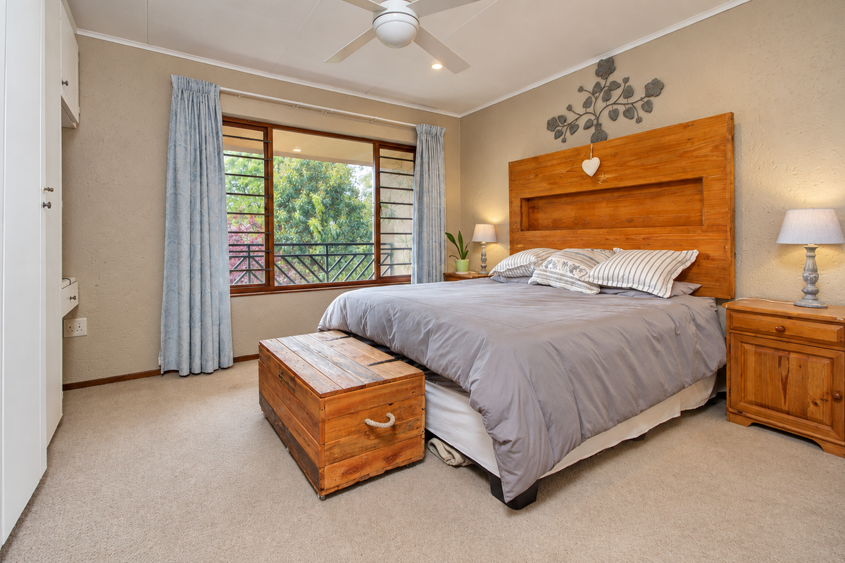 A well-maintained bedroom featuring neutral walls, carpeted flooring, a ceiling fan, and a built-in wardrobe with access to a balcony view.