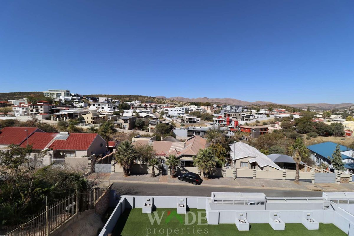 Elevated aerial view overlooking a residential neighbourhood with surrounding hills, featuring a foreground terrace with artificial turf and perimeter walling.