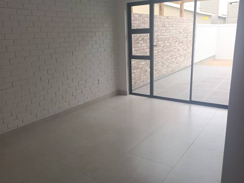 An empty living room featuring a painted brick feature wall, large format floor tiles, and a sliding door providing access to the rear patio.