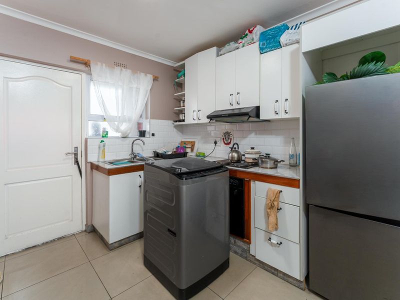 Compact kitchen featuring white cabinetry, tiled backsplash, built-in oven, extractor fan, and tiled flooring, providing a functional workspace.