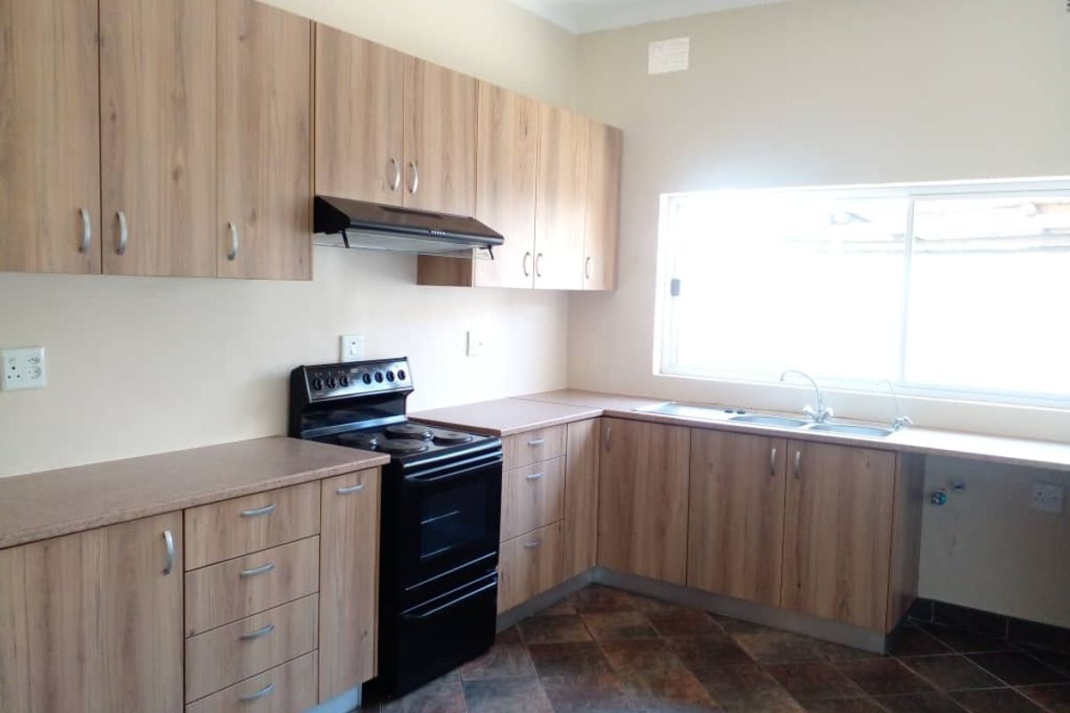 A clean, functional kitchen featuring light wood-tone cabinetry, laminate countertops, a freestanding stove with extractor fan, and tiled flooring.