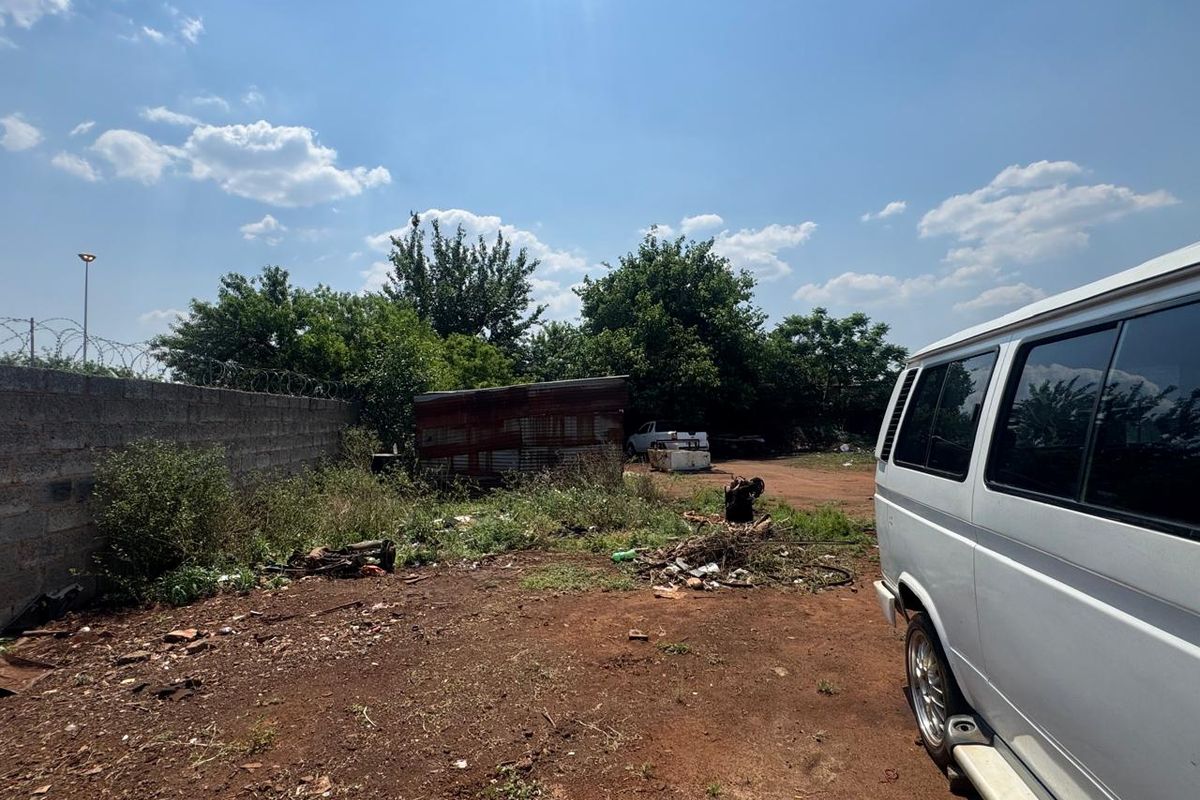 An undeveloped rear exterior area featuring a perimeter wall with razor wire security and a small metal storage structure.