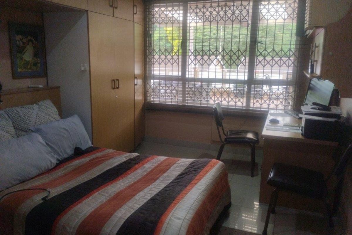 A functional bedroom featuring built-in cupboards, tiled flooring, and a window fitted with a security gate for added protection.