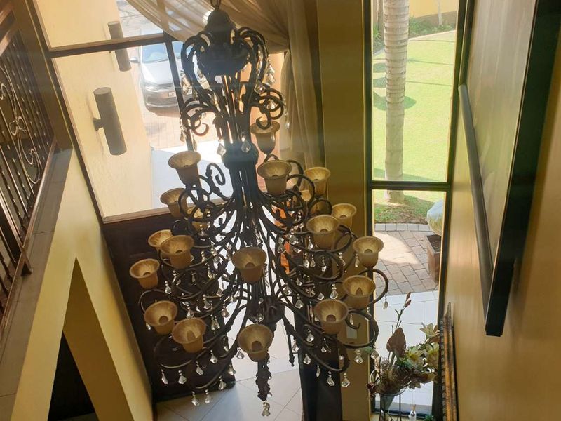 A grand entrance hall featuring a large ornate wrought iron chandelier, high ceilings, and expansive windows overlooking the front garden.