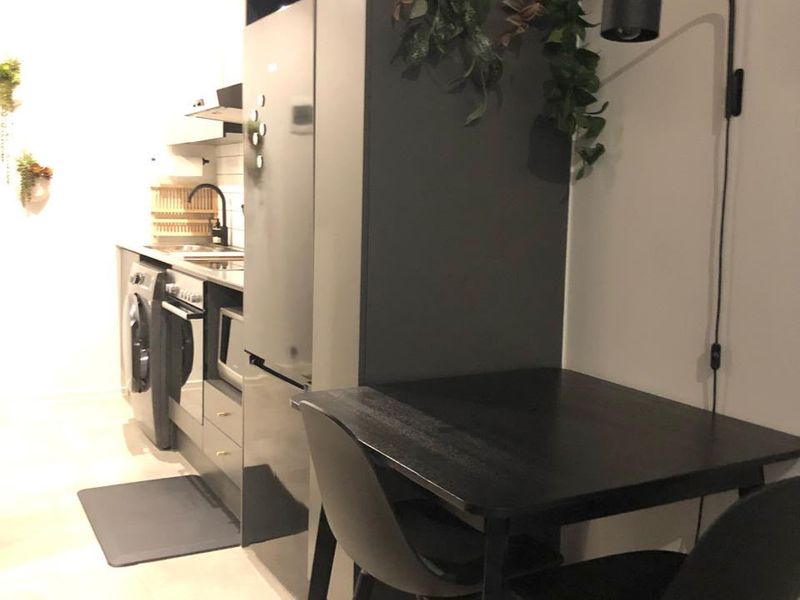 A modern, compact kitchen featuring dark cabinetry, integrated appliances, and tiled flooring, with a small dining area adjacent to the main workspace.