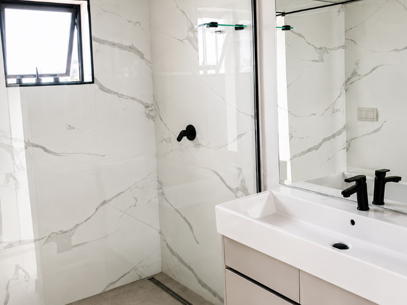 Modern bathroom featuring a walk-in shower with marble-look tiling, a floating vanity with a black matte faucet, and a large wall mirror.