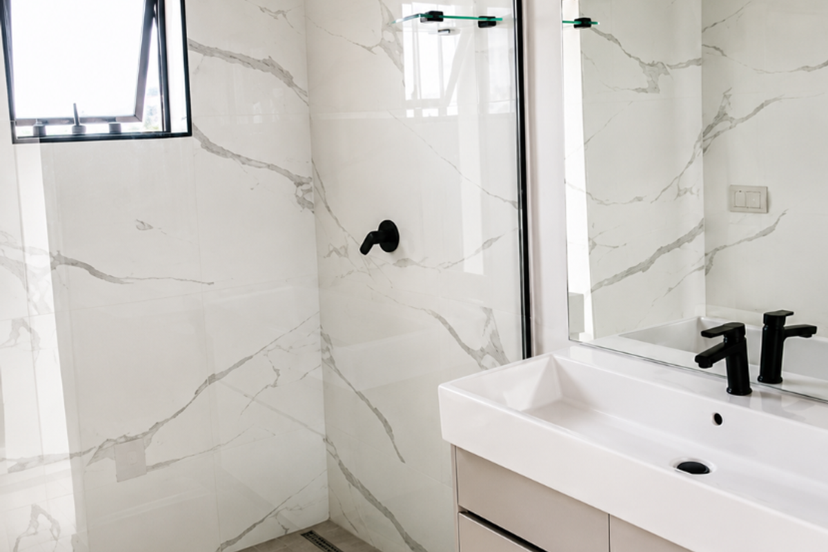 Modern bathroom featuring a walk-in shower with marble-look tiling, a floating vanity with a black matte faucet, and a large wall mirror.