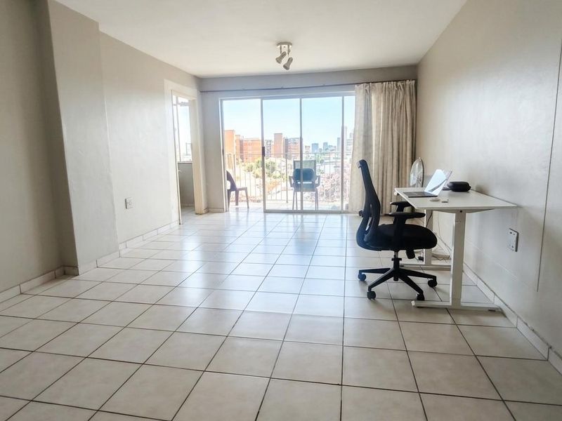 Spacious living area featuring neutral tiled flooring and large sliding glass doors that provide access to a balcony with city views.