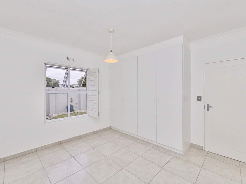 A bright, empty bedroom featuring neutral tiled flooring, built-in cupboards, and a window with shutter, offering a clean and versatile living space.