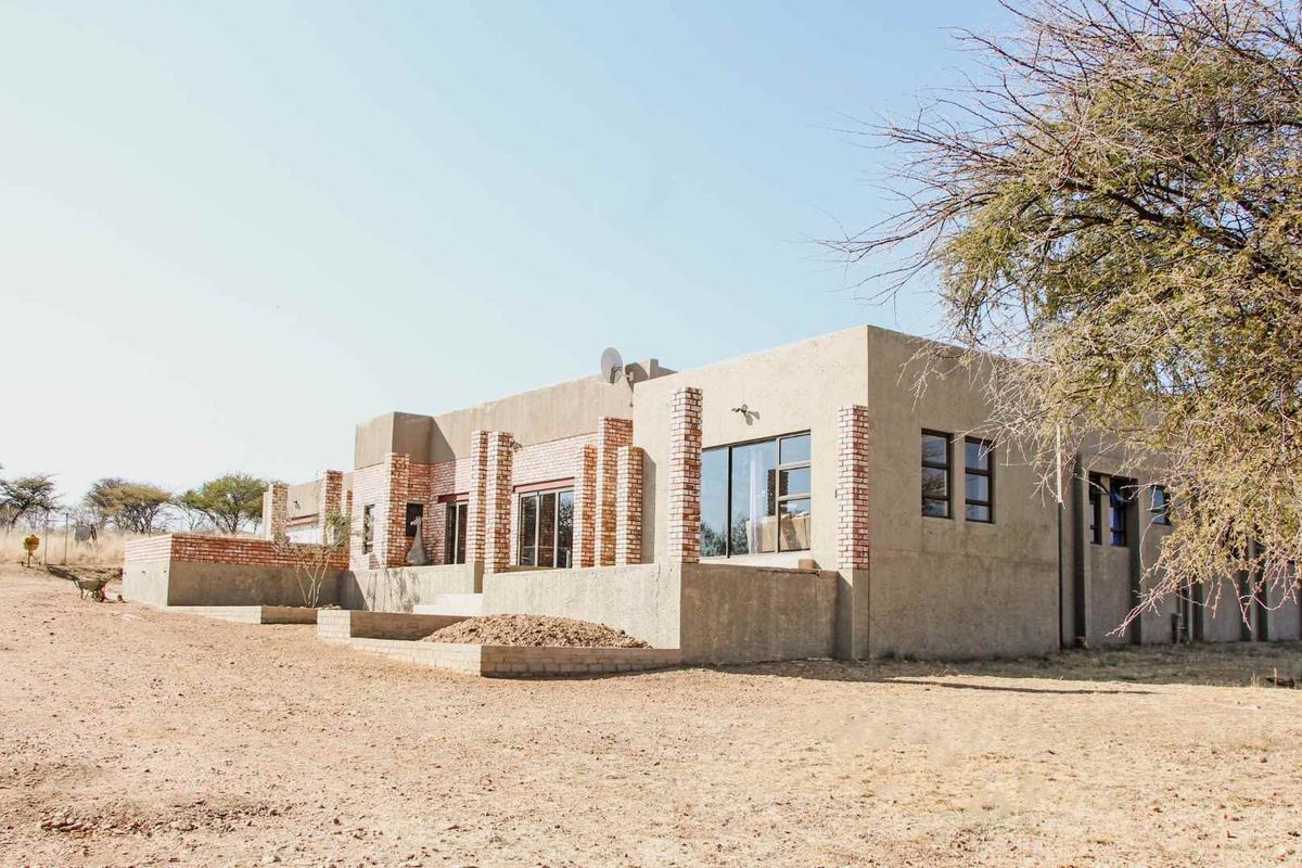 Rear view of a single-story house featuring exposed brick columns, plastered walls, and sliding glass doors, set on an unlandscaped plot.