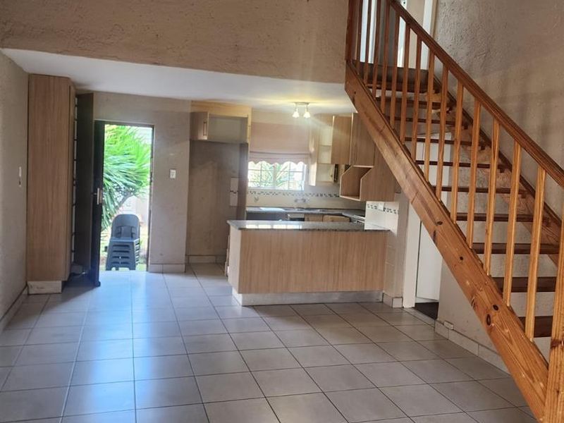 Open plan living and kitchen area featuring tiled floors, a wooden staircase, and functional kitchen cabinetry with an island.