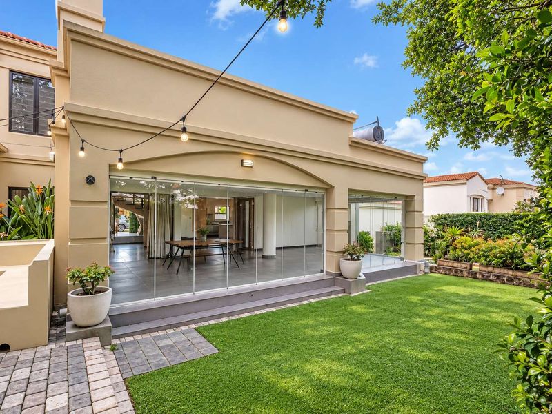 A well-maintained rear exterior featuring a paved garden, manicured lawn, and a covered patio enclosed by modern stacking glass doors.