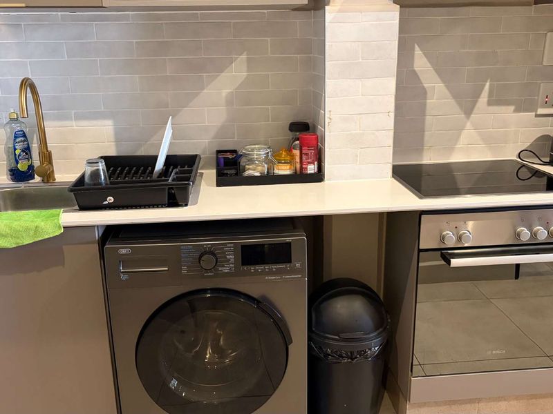 A modern kitchen featuring a subway tile backsplash, quartz countertops, brass faucet, built-in oven, electric cooktop, and an integrated washing machine.