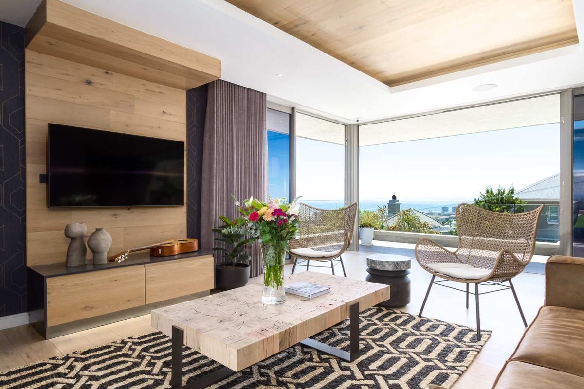 Modern living room featuring timber ceiling accents, built-in media cabinetry, and expansive sliding glass doors opening to a scenic outdoor balcony.