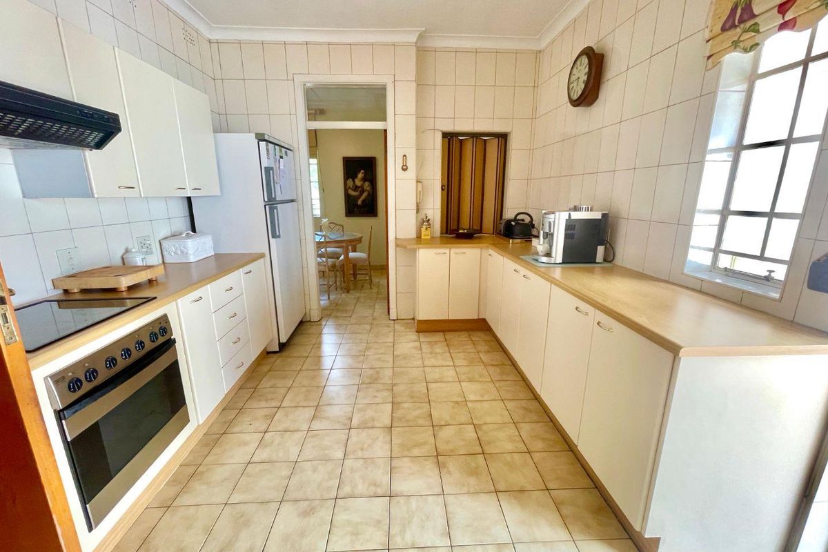 A functional kitchen featuring white cabinetry, laminate countertops, built-in oven, hob, and extractor fan, with full-height wall tiling and tiled flooring.