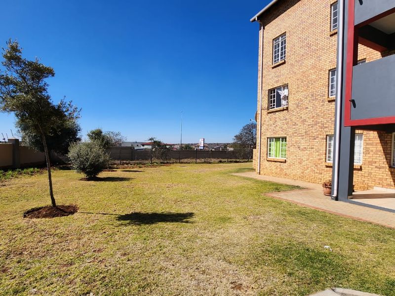 A view of the rear exterior of the apartment building, featuring a face brick facade, a paved patio area, and a spacious communal garden.