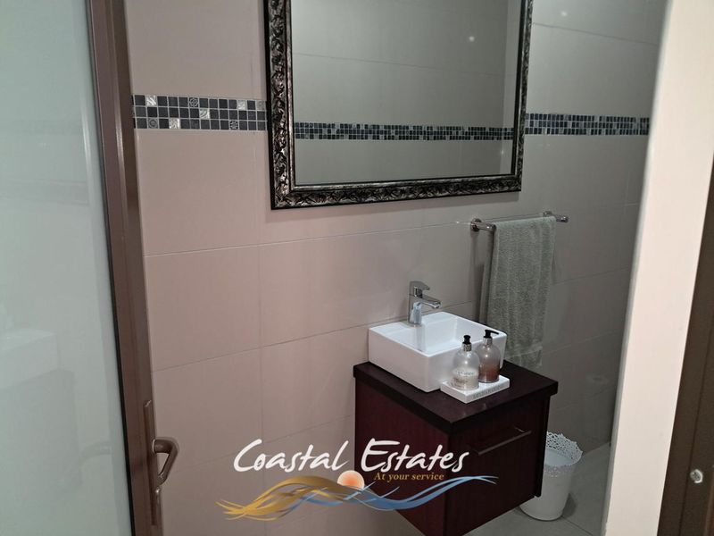A modern bathroom featuring a wall-mounted vanity with a vessel sink, chrome mixer tap, and a decorative mosaic-tiled wall accent.
