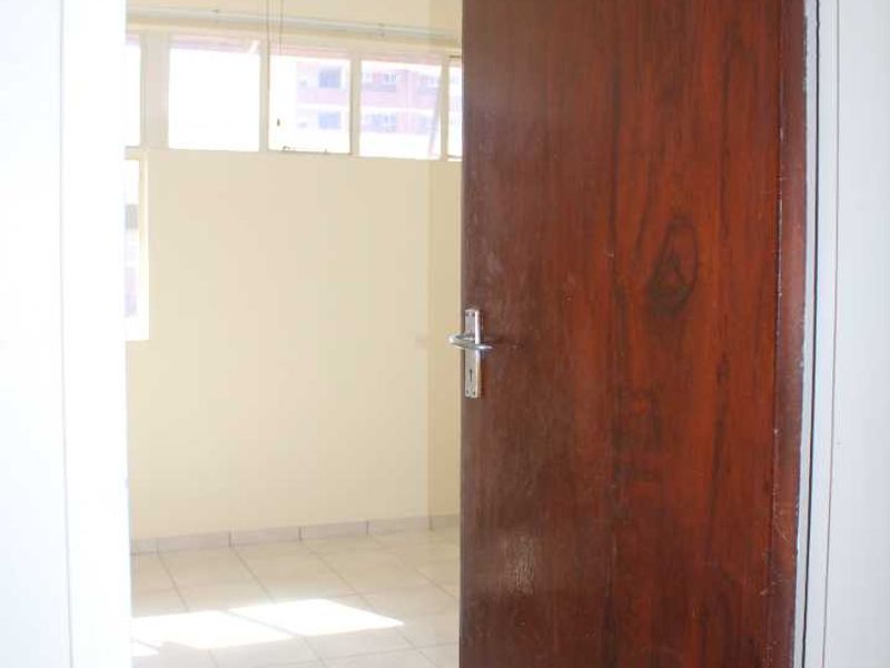 An empty bedroom featuring tiled flooring, a ceiling fan, and large windows, viewed through an open timber door.