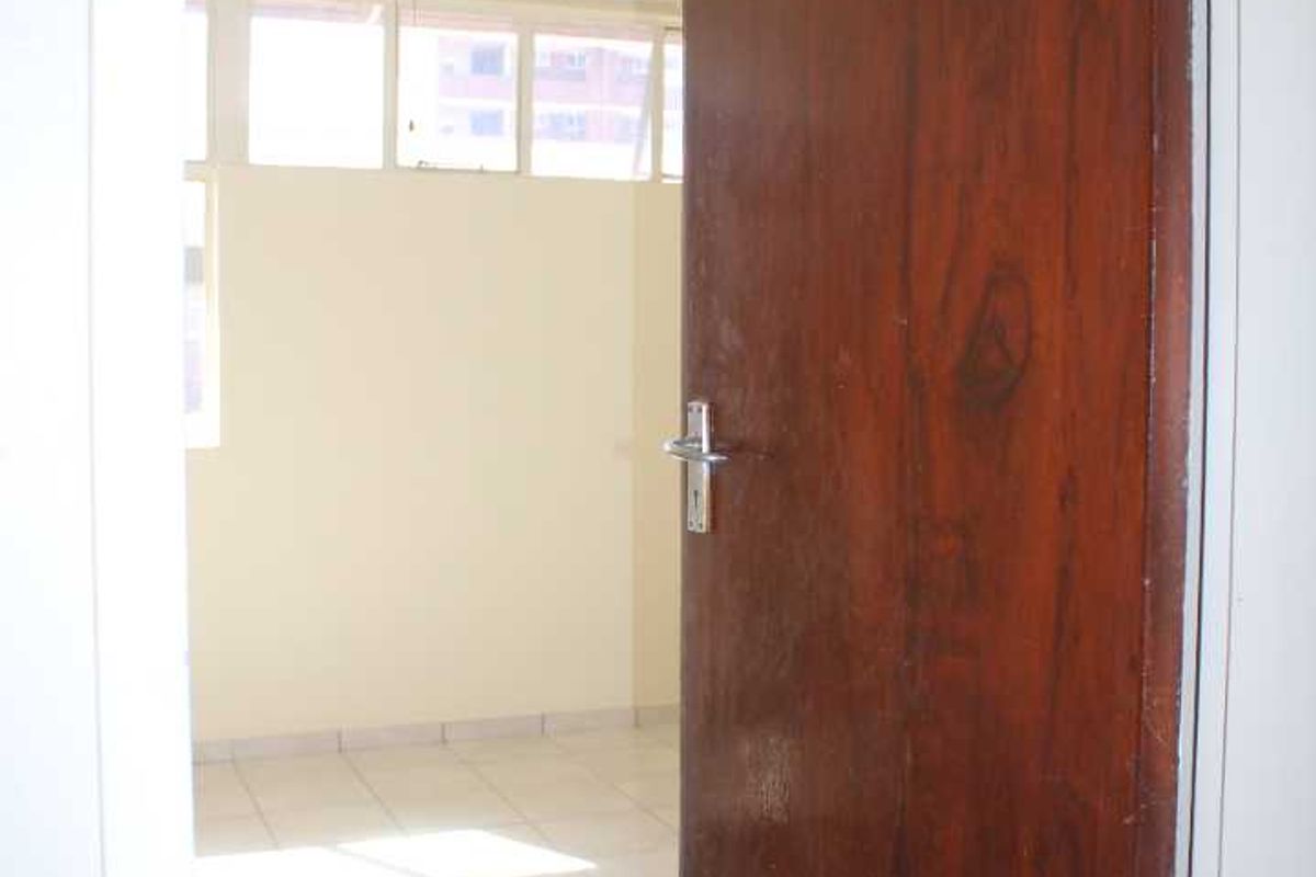 An empty bedroom featuring tiled flooring, a ceiling fan, and large windows, viewed through an open timber door.
