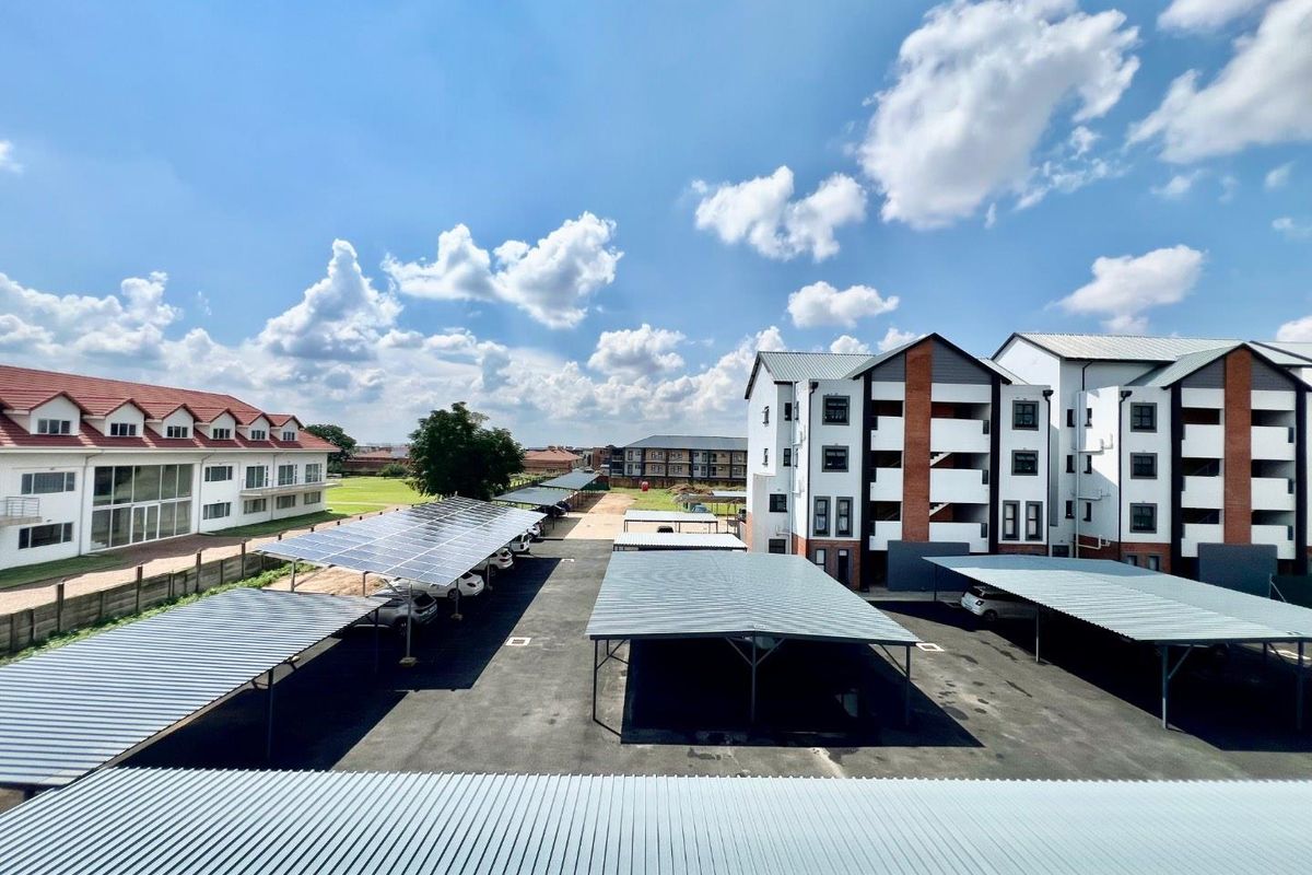 An elevated view of the apartment complex grounds, featuring paved parking areas with covered carports and solar panel installations.