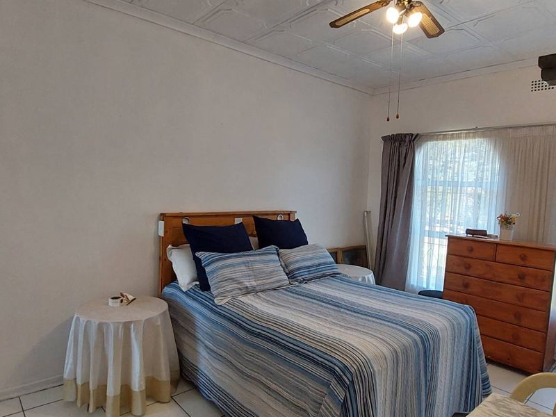 A bedroom featuring tiled flooring, a ceiling fan, and distinctive arched windows with natural light.