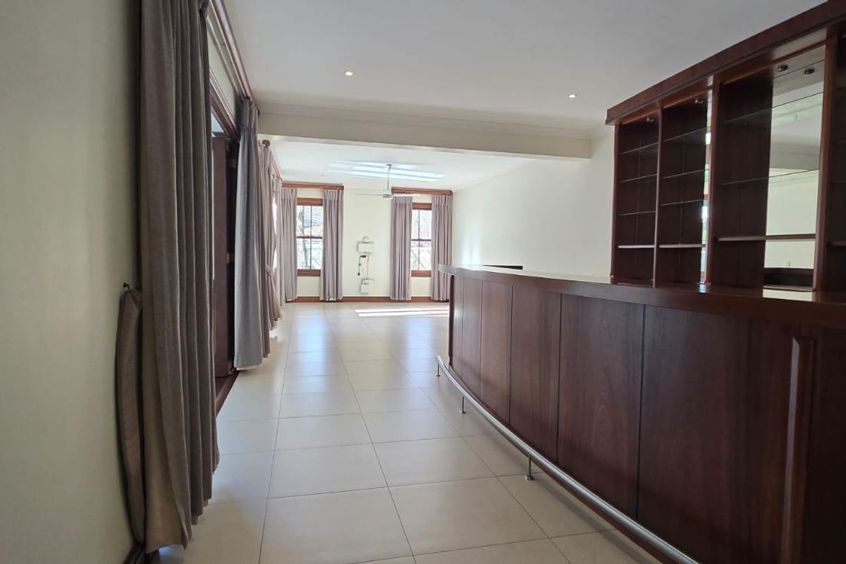 Spacious living area featuring a built-in wooden bar with shelving, tiled flooring, and large windows allowing for natural light.