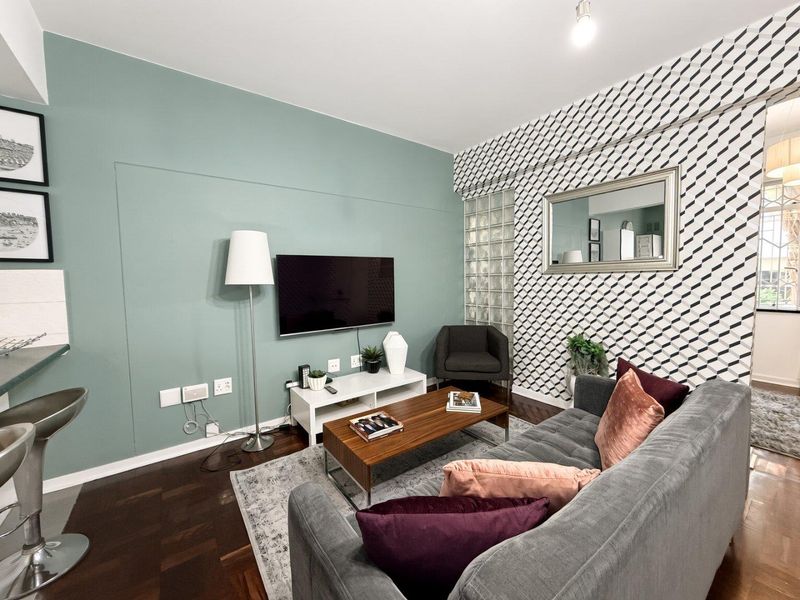 A well-maintained living room featuring hardwood flooring, a decorative glass block feature wall, and a modern accent wall with integrated television mounting.