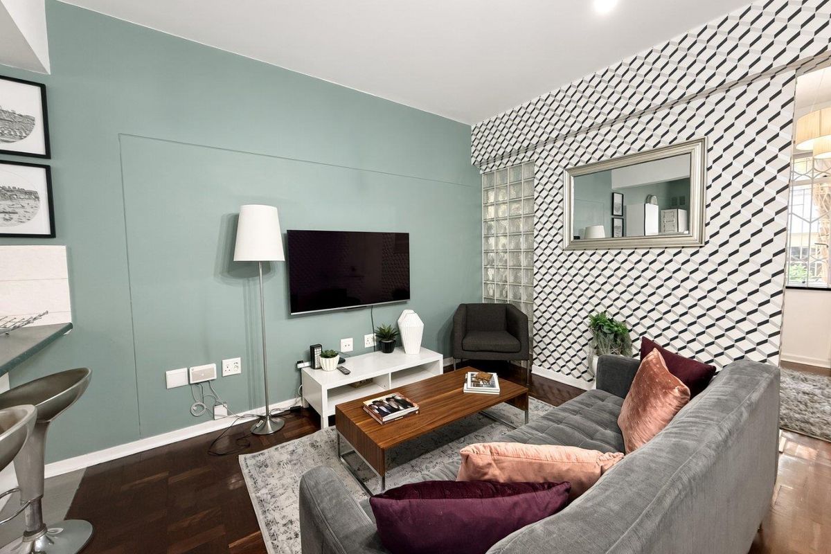 A well-maintained living room featuring hardwood flooring, a decorative glass block feature wall, and a modern accent wall with integrated television mounting.