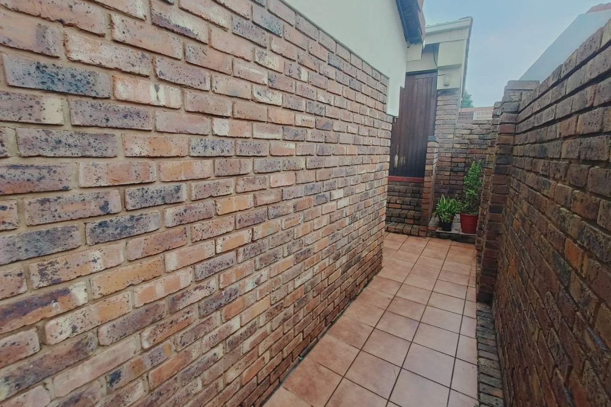 A narrow exterior side passage featuring face-brick walls and tiled flooring, leading towards a rear entrance area.