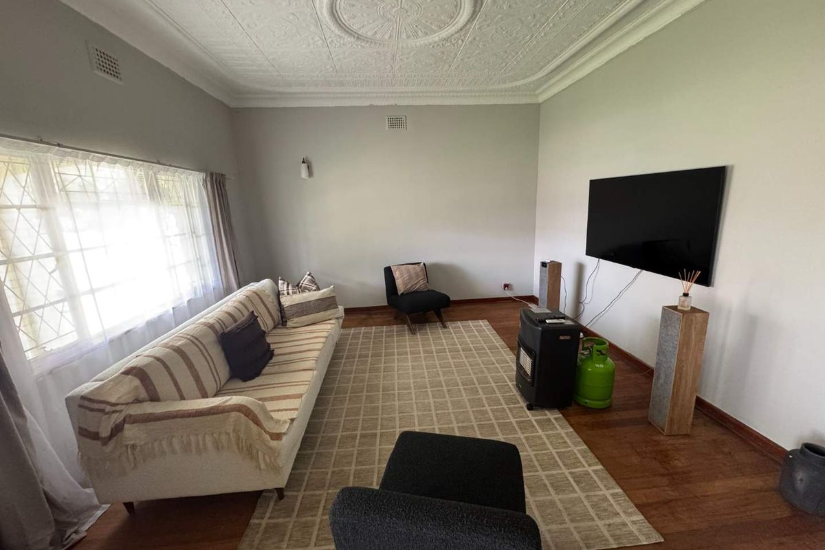 A living room featuring original decorative pressed metal ceilings, timber flooring, and large windows allowing for natural light.