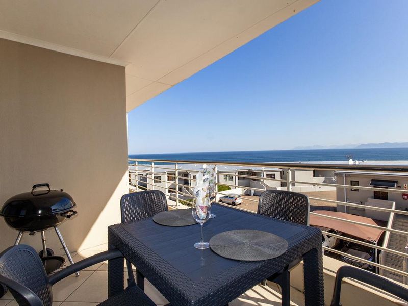 A spacious covered balcony featuring tiled flooring and a metal balustrade, offering expansive ocean views.