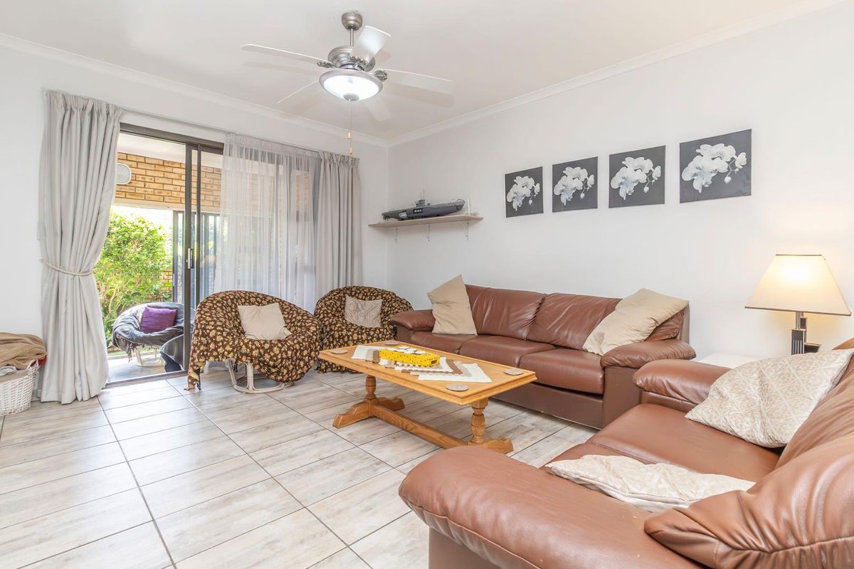 A bright living room featuring tiled flooring, a ceiling fan, and large sliding glass doors that open onto a covered patio area.