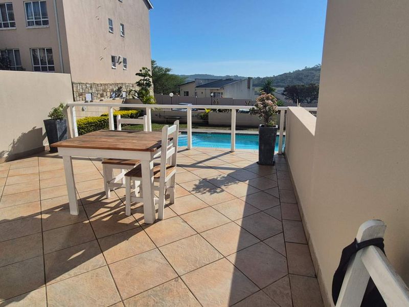 A spacious outdoor balcony featuring tiled flooring and a protective railing, offering a clear view of the complex swimming pool area.
